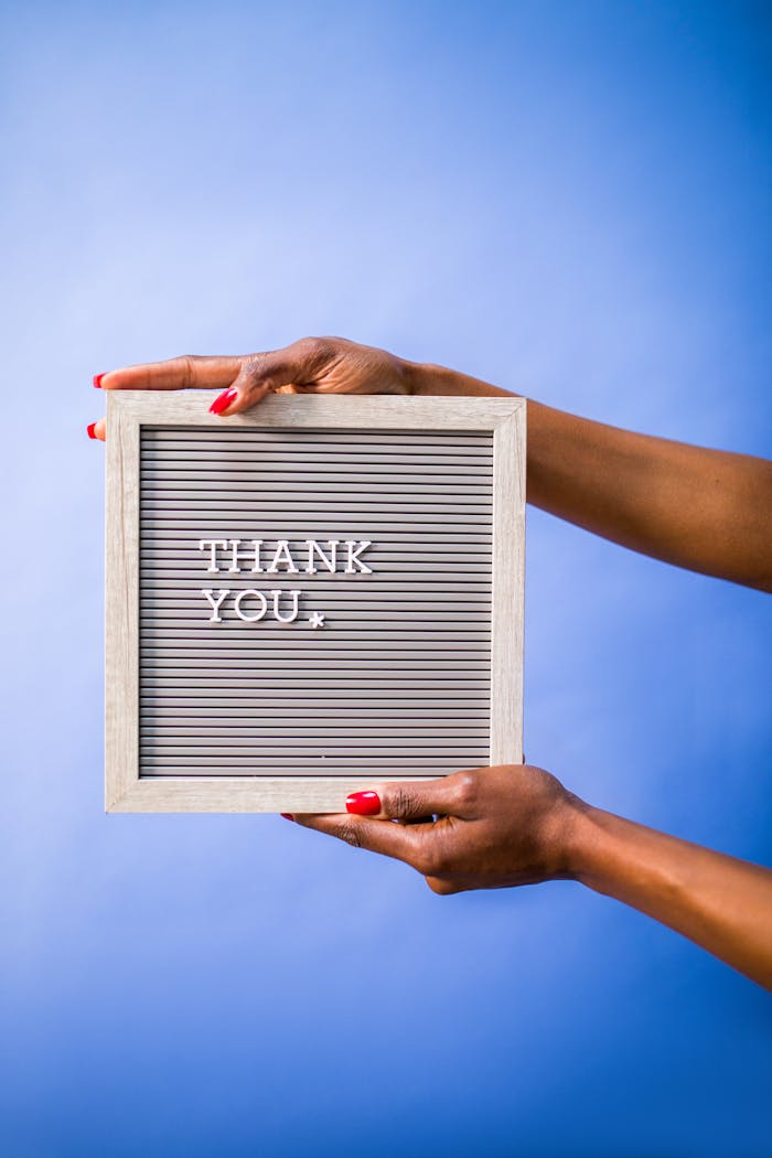 Hands holding thank you sign on blue backdrop, perfect for social media and digital marketing.